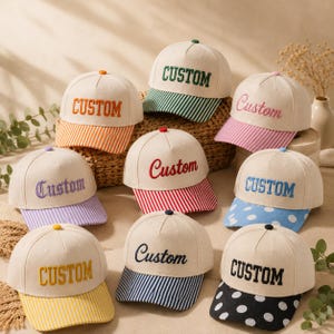 May include: A collection of nine baseball caps with off-white crowns and various colored brims. Each cap features the word Custom embroidered on the front in different fonts and colors, including striped and polka-dot patterns on the brims.