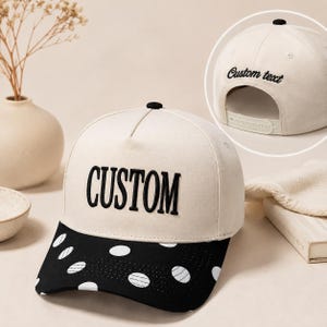 May include: A cream-colored baseball cap with a black brim featuring white polka dots. The front panel displays the word CUSTOM in black embroidered lettering. A circular inset shows the back of the cap with the embroidered text Custom text.
