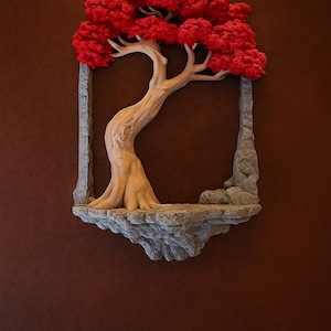 Op de afbeelding: Een 3D-wandkunstwerk met een gestileerde boom met een rode, getextureerde luifel en een lichtbruine stam. De boom staat in een grijs, steenachtig frame, gemonteerd op een bruine muur. Het kunstwerk roept een natuurlijk thema op.
