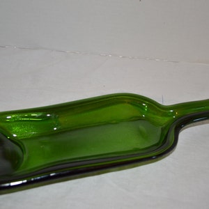 May include: A green glass bottle that has been flattened and reshaped into a serving tray. The tray is a vibrant green color and has a smooth, glossy finish. The tray is designed to resemble the shape of a wine bottle.
