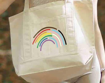 May include: A large, off-white canvas tote bag featuring a graphic of a stylized rainbow. The rainbow design consists of several curved, segmented lines in various colors including brown, black, red, orange, yellow, green, blue, and purple.