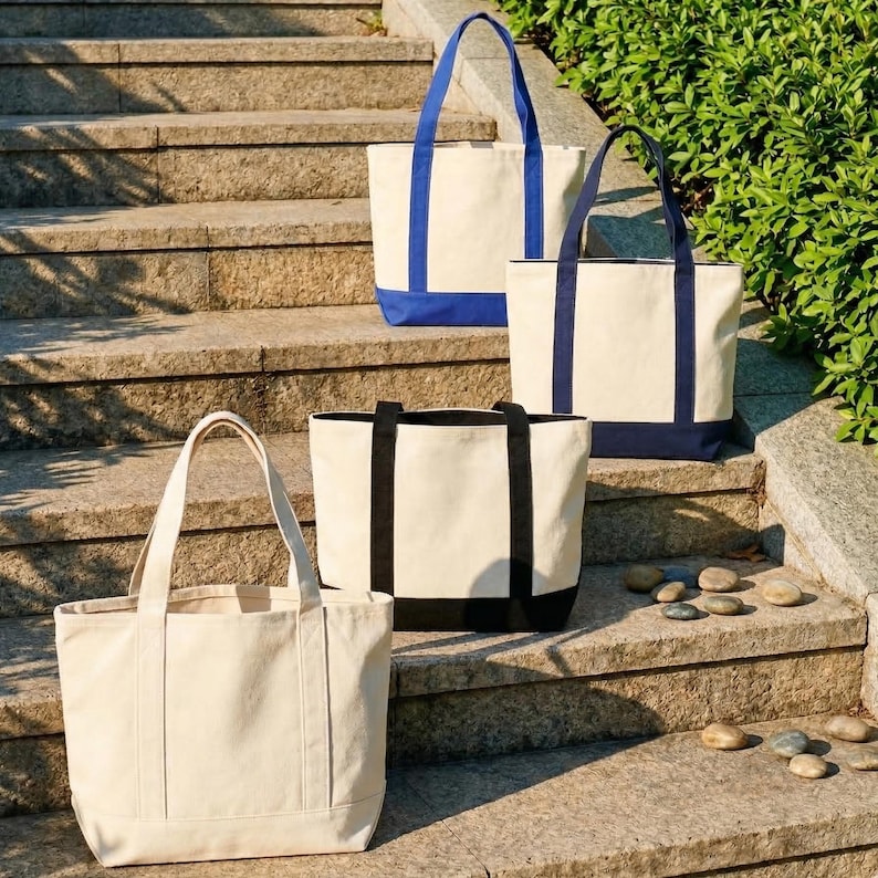 Puede incluir: Cuatro bolsas de mano de lona de diferentes tama&ntilde;os y dise&ntilde;os se muestran en escalones de piedra. Las bolsas tienen tela color crema con detalles en azul y negro. Las bolsas tienen asas resistentes.