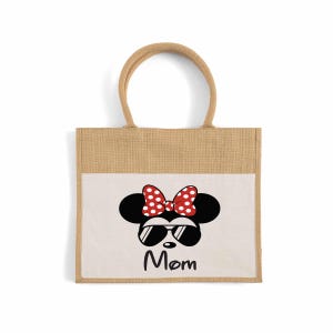 May include: A rectangular tote bag made of natural tan jute fabric with two matching handles. The front features a white panel printed with a black silhouette of a mouse head wearing red polka-dot bow and black sunglasses, with the word Mom below.