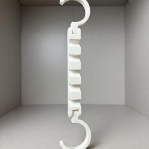May include: A white plastic space-saving hanger with a hook at the top and bottom. The hanger has a series of rectangular slots for multiple garments. The design is intended to maximise wardrobe space.