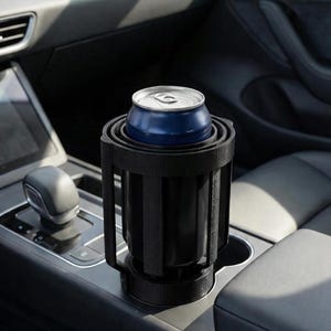 Könnte beinhalten: Ein schwarzer Getränkehalter für das Auto mit einer blauen Dose darin. Der Getränkehalter ist so konzipiert, dass er in den vorhandenen Getränkehalter eines Autos passt. Der Innenraum des Autos ist im Hintergrund zu sehen.
