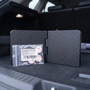 May include: Black car trunk organizer with a textured surface, shown open. A small bag of round, red and white adhesive fasteners is in front of the organizer. The text on the bag reads "Round 20mm Dual Lock 3M SJ3550".