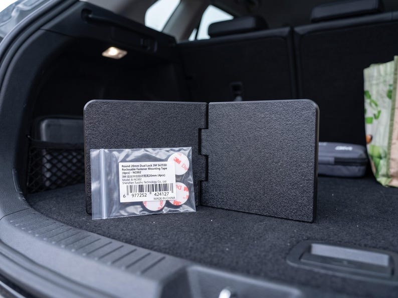 May include: Black car trunk organizer with a textured surface, shown open. A small bag of round, red and white adhesive fasteners is in front of the organizer. The text on the bag reads "Round 20mm Dual Lock 3M SJ3550".