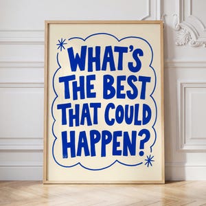 May include: A framed poster with the text "WHAT'S THE BEST THAT COULD HAPPEN?" in blue, outlined in a cloud-like shape, on a cream background. The poster is in a light wood frame and stands on a wooden floor.