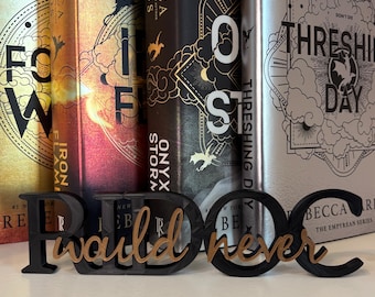 Può includere: Quattro libri con copertina rigida di Rebecca Yarros con copertine metalliche color oro, rame, nero e argento sono disposti in verticale. Davanti si trova un'insegna in legno nero e beige con il testo in corsivo "I would never".
