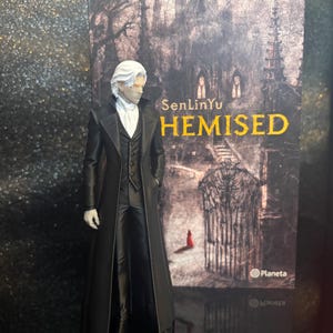 Puede incluir: Una figura de un personaje con cabello blanco que viste un abrigo largo negro, un chaleco negro y una corbata blanca, frente a la portada de un libro titulada SenLinYu THEMISED con la ilustraci&oacute;n de un castillo oscuro y una peque&ntilde;a figura roja.