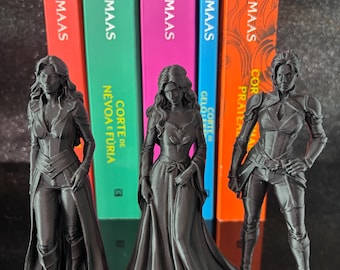 Può includere: Tre statuette monocromatiche nere in piedi davanti a cinque dorsi di libri colorati di Sarah J. Maas. La figura a sinistra indossa un cappotto lungo, quella centrale un abito lungo e quella a destra un'armatura aderente con stivali.