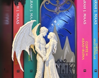Può includere: Una statuetta testurizzata di colore chiaro raffigurante una figura maschile alata e una figura femminile con un abito lungo, posizionate davanti a un pannello decorativo blu scuro, ad arco, stampato in 3D con un design di montagne e stelle.