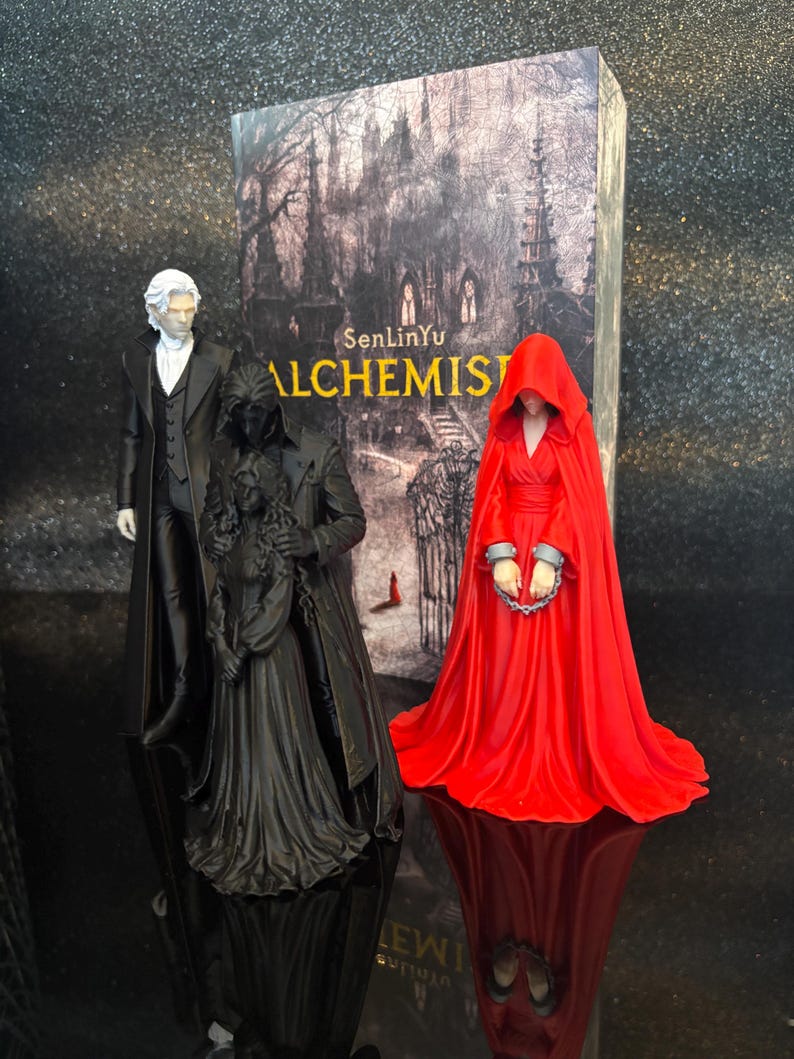 Puede incluir: Tres figuras se encuentran frente a un libro titulado SenLinYu ALCHEMIST. Una figura viste traje negro y camisa blanca. Otra es una figura vestida de negro que sostiene a una persona con vestido largo. La tercera lleva una capa roja con capucha y grilletes.