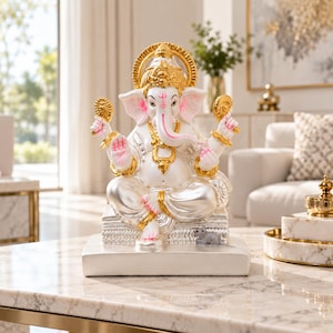 Pode incluir: Uma estátua branca e dourada da divindade Ganesha sentada em posição de lótus sobre uma base retangular. A figura apresenta uma cabeça de elefante proeminente, quatro braços e uma pequena figura de rato posicionada na base do pedestal.