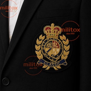 Puede incluir: Un blazer negro con una camisa blanca de cuello debajo y un destacado escudo bordado en el pecho. El escudo muestra una corona dorada, espigas de trigo y un escudo central con el texto MCMLXVII y la palabra CLASSIC debajo.