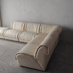 May include: A large off-white sectional sofa with a modular design. The sofa is made of a soft, plush fabric and has a contemporary style.