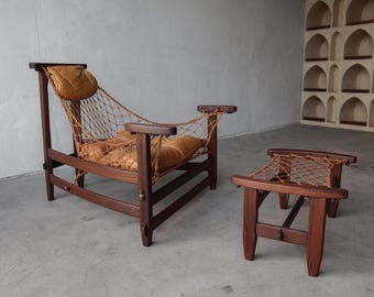 May include: A wooden armchair and matching footstool set. The chair features a brown wooden frame, a woven net back and seat, and tan leather cushions. The footstool has a similar design. The set is in a neutral-toned room.