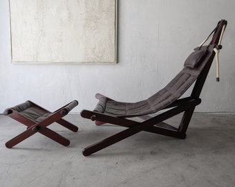 May include: A dark brown wooden folding chair with a gray canvas seat and a matching footrest. The chair has a rope detail and a small gray pillow.