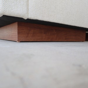 May include: A white fabric sofa with a wooden base. The base is a dark brown color and has a rectangular shape.