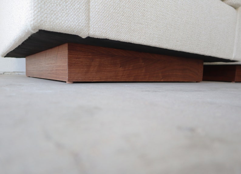 May include: A white fabric sofa with a wooden base. The base is a dark brown color and has a rectangular shape.