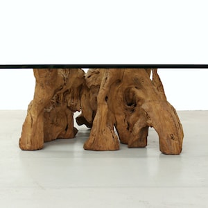 May include: A coffee table with a glass top and a unique base made of natural wood with a rough, organic texture.