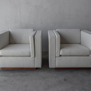 May include: Two light gray upholstered armchairs with a wood base. The chairs have a simple, modern design.