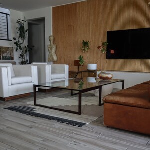 May include: A living room with a brown leather sofa, two white armchairs, a glass coffee table, and a wooden wall with a flat screen TV.