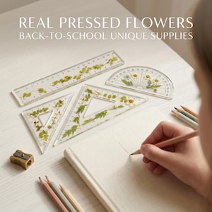 Könnte beinhalten: Ein Set aus transparenten Geometrie-Werkzeugen, bestehend aus einem Lineal, zwei Geodreiecken und einem Winkelmesser, die mit echten gepressten Blumen und grünen Blättern gefüllt sind. Der Text REAL PRESSED FLOWERS BACK-TO-SCHOOL UNIQUE SUPPLIES ist sichtbar.