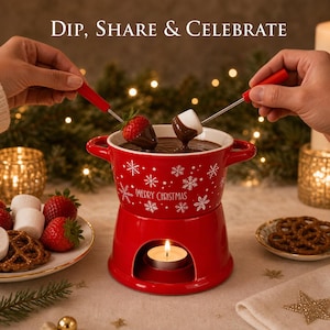 Puede incluir: Una olla de fondue de cerámica roja con patrones de copos de nieve blancos y el texto "Merry Christmas" impreso en el frente. La olla se asienta sobre una base roja a juego con una vela encendida, mientras dos tenedores de metal sumergen una fresa y un malvavisco.