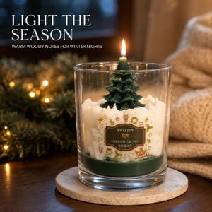 Peut inclure: Une bougie dans un récipient en verre transparent contenant de la cire blanche et une figurine en forme de sapin vert foncé. L'étiquette sur le verre porte l'inscription "Xmas JOY" et "WARMTH FOR THE HOLIDAYS" entourée de petits motifs festifs.