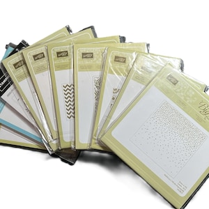 May include: A collection of Stampin' Up! embossing folders and die-cutting plates, including a Big Shot folder. The folders are in clear plastic packaging with various designs, including a chevron pattern and a dotted design.