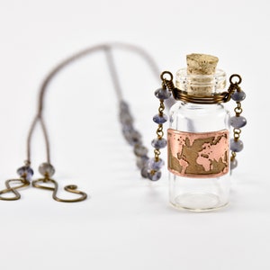 Könnte beinhalten: Eine Halskette mit einer Glasflasche, einem Korkverschluss und einem kupfernen Weltkartenmotiv. Die Kette besteht aus einem braunen Band und blauen Perlen.