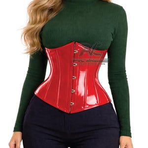 May include: A glossy red corset with a structured design. The corset features a series of metal clasps down the front and is worn over a dark green turtleneck. The text "PVC DREAMS PREMIUM HANDMADE CRAFTS" is visible.