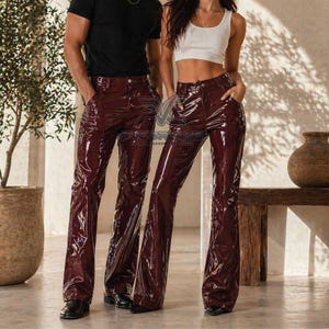 Può includere: Pantaloni in vinile bordeaux con gamba svasata. I pantaloni hanno una finitura lucida e un classico design a cinque tasche. I pantaloni sono indossati con una t-shirt nera e un top corto bianco.