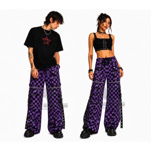 May include: A black t-shirt with a red star graphic and a black crop top. The image features purple and black checkered wide-leg trousers with silver hardware and zippers. The trousers have straps with silver grommets.