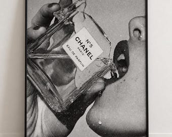 May include: A black and white framed wall art print depicting a person pouring a glass bottle of Chanel N°5 Eau de Parfum into their mouth. The image features a grainy, vintage aesthetic with visible liquid droplets and clear glass textures.