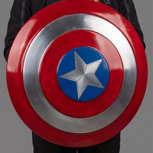 May include: A large, round shield in red, silver, and blue. The shield has a central blue circle with a silver star, surrounded by silver and red bands. A prop or collectible item.