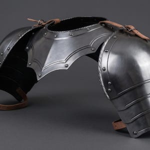 May include: Polished steel shoulder armour with riveted construction and leather straps. The armour is designed to protect the shoulders and upper chest, with articulated plates for flexibility.