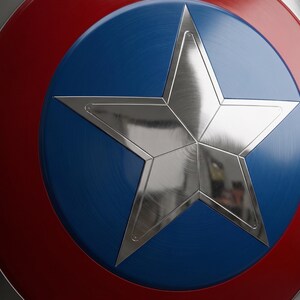 May include: A close-up of a shield featuring a silver star on a blue disc, encircled by a red band. The shield has a metallic finish, reflecting light. The design is reminiscent of a superhero's emblem.