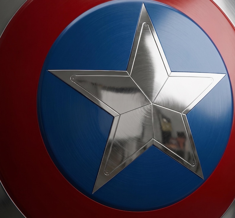 May include: A close-up of a shield featuring a silver star on a blue disc, encircled by a red band. The shield has a metallic finish, reflecting light. The design is reminiscent of a superhero's emblem.