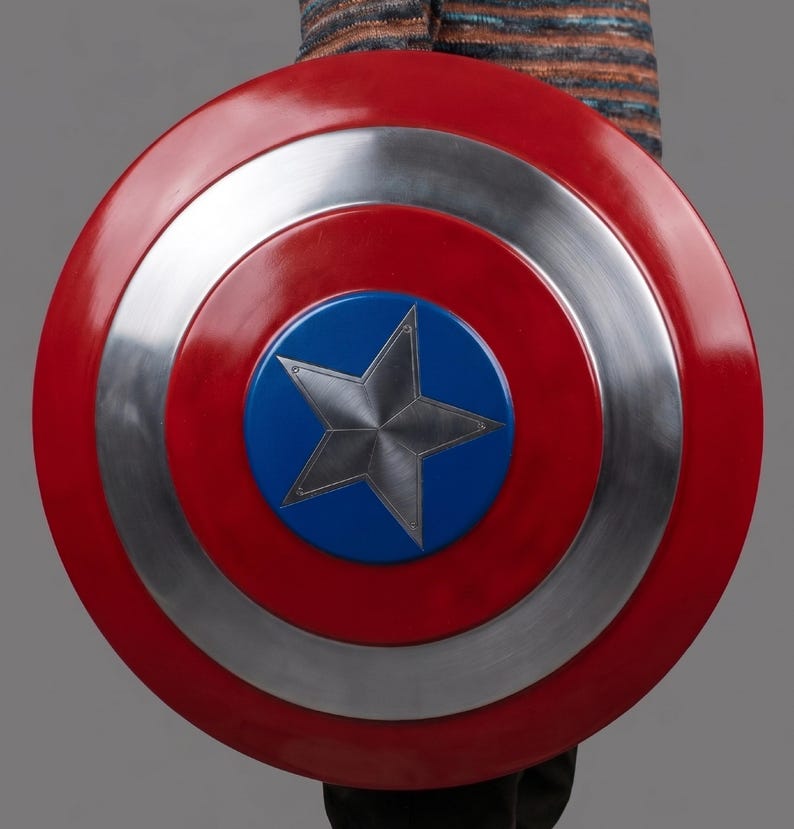 May include: A circular shield in red, silver, and blue. The shield has a central blue circle with a silver star. The outer ring is red, followed by a silver ring, and then another red ring. The shield is held by a person.