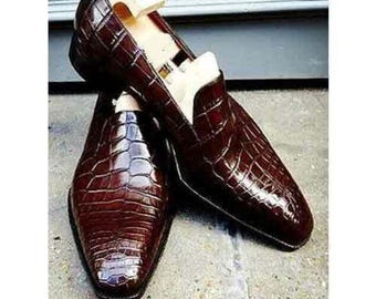 Peut inclure: Une paire de mocassins marron foncé avec un motif texturé en peau de crocodile brillant. Chaque chaussure présente un bout pointu et est équipée d'un embauchoir en bois clair pour maintenir la forme de la structure de la chaussure.