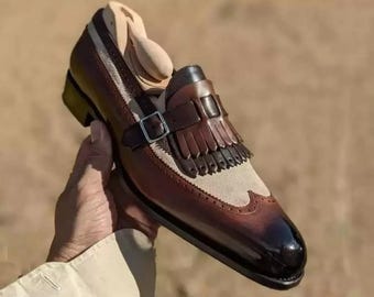 Peut inclure: Un mocassin en cuir bicolore avec un bout et un talon brun foncé patiné, une empeigne en daim beige et un panneau à franges décoratif. La chaussure comprend une bride en cuir brun foncé avec une boucle en métal argenté sur le cou-de-pied.