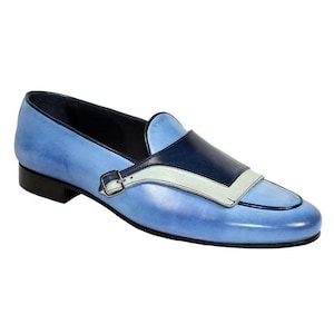 May include: A light blue leather loafer with a dark blue and white accent design. The shoe features a small silver buckle and a black sole. The overall design is stylish and modern.