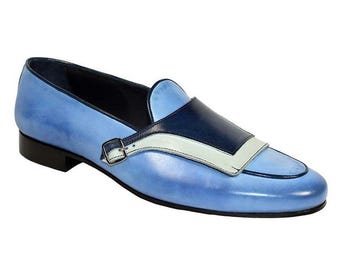 Peut inclure: Mocassin en cuir bleu clair avec un motif bleu foncé et blanc. La chaussure est ornée d'une petite boucle argentée et d'une semelle noire. Le design est élégant et moderne.