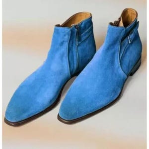 Op de afbeelding: Een paar felblauwe suède enkellaarsjes met een spitse neus, een ritssluiting aan de zijkant en een lage hak. De laarsjes hebben een gladde, uniforme textuur en een strak silhouet met een riempje bij de schacht van de enkel.
