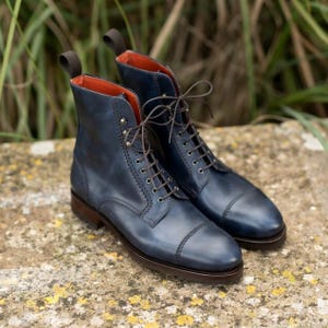 Op de afbeelding: Een paar marineblauwe leren veterschoenen met een neuskap, donkerbruine veters, zilverkleurige oogjes, een hiellus en een feloranje binnenvoering, geplaatst op een donkerbruine gestapelde hak en zool.