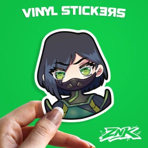 May include: A vinyl sticker featuring a cartoon character with short dark hair, green eyes, and a black mask. The character is wearing a green and yellow outfit. The sticker has a white border and the text "VINYL STICKERS" is above the character.