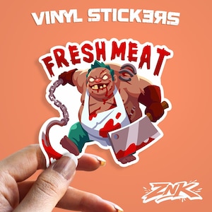May include: A vinyl sticker featuring a cartoon butcher with a cleaver and chain, with the words "FRESH MEAT" in red. The sticker has a white border and is held against an orange background. The text "VINYL STICKERS" is at the top.