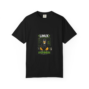 May include: Black t-shirt featuring a graphic of a penguin using a laptop with the text "LINUX - IS USER FRIENDLY" above and "BUT ROOT IS EVERYWHERE" below. The penguin is wearing a hoodie. The shirt is a crew neck.